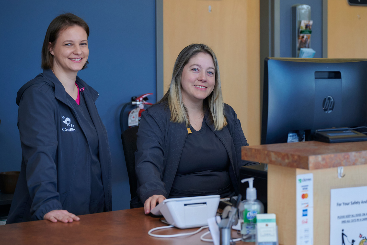 This image depicts two vets smiling behind a front desk.