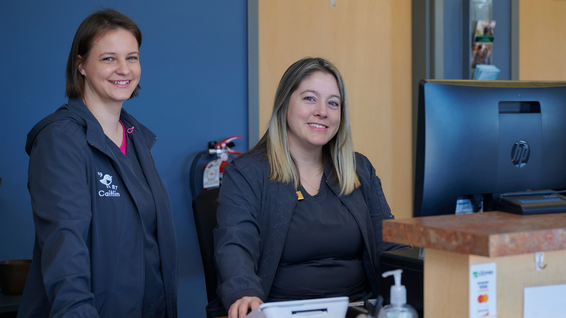 This image depicts two vets smiling behind a front desk.